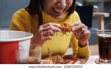Young Asian woman happily eating fried chicken inside home celebrating the weekend.