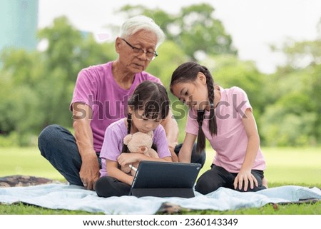 Happy Asian family children using tablet with her grandfather in the park
