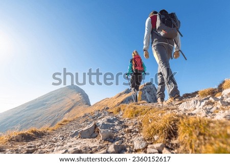 Spectacular view of two hikers walking along the mountain ridge route with the sun on the clear blue sky, aerial shot. Inspiration, nature, and mountaineering concepts. Royalty-Free Stock Photo #2360152617