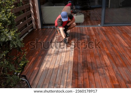 Wood worker applying nourishing deck oil with paintbrush on cleaned and sanded Ipe decking terrace boards Royalty-Free Stock Photo #2360178917