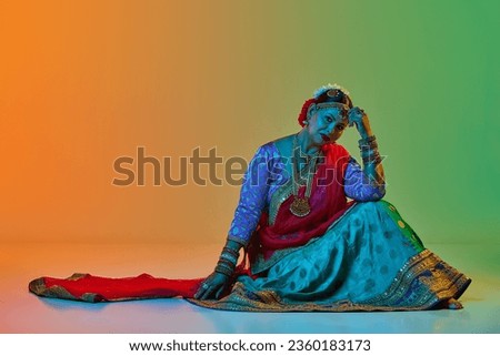 Indian culture. Mature, beautiful indian woman in traditional clothes, dress posing over gradient studio background in neon light. Concept of beauty, fashion, India, traditions, choreography, art. Ad