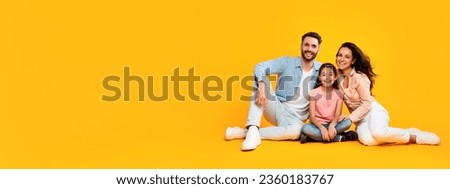 Smiling happy european parents sitting on the floor with their child girl, posing on yellow color background, panoramic shot, free copy space, banner
