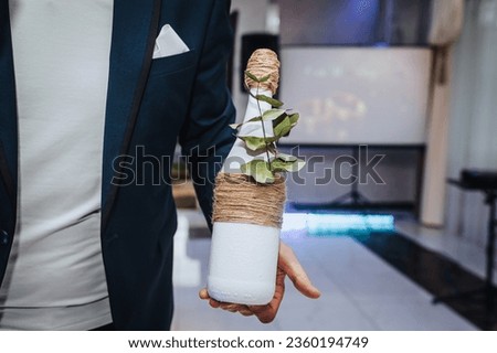 The man leading holds a decorated bottle of champagne in his hands at a holiday, wedding, birthday. Close-up photography, gift, tradition, design.