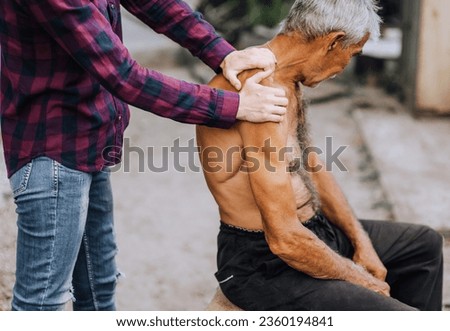 An adult woman, a professional doctor, makes a relaxing massage with her hands to a sick old elderly gray-haired retired man with scoliosis on his back. Photography, close-up portrait.