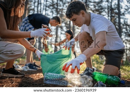 group of teenage friends gen Z male and female caucasian men women picking up waste garbage plastic bottles and paper from the forest cleaning up nature in sunny day environmental care ecology concept Royalty-Free Stock Photo #2360196939