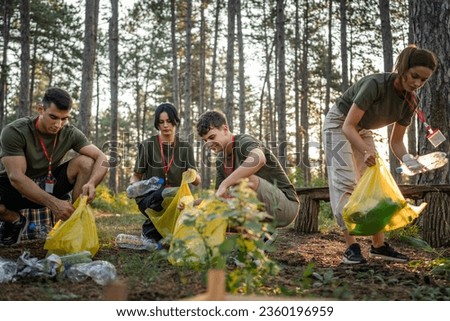 group of teenage friends gen Z male and female caucasian men women picking up waste garbage plastic bottles and paper from the forest cleaning up nature in sunny day environmental care ecology concept Royalty-Free Stock Photo #2360196959