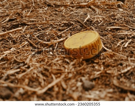 Picture of a yellow bottle cap on a dry field.
