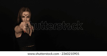 The witch points to the camera lens with a finger with long red nails. Copy space. A woman dressed as a witch for halloween points her finger at you. Halloween holiday concept. Place to insert text.