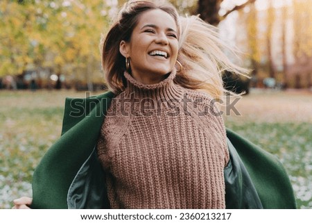 Girl in motion expressing happiness at city park. Attractive, cheerful woman running, feeling free and joyful during the nice autumn day.