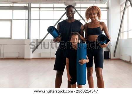 african american young family standing together in the gym and holding yoga mat, father mom and son on fitness training with karemat in black sportswear