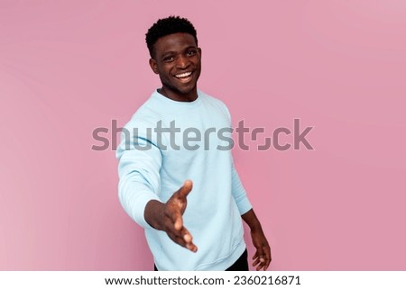 african american man in blue sweater gives his hand on pink isolated background, man makes handshake and says welcome Royalty-Free Stock Photo #2360216871