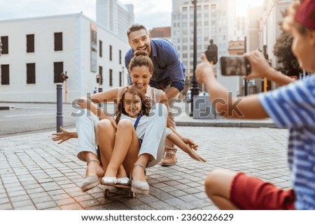 Young family having fun with a skateboard in the city and taking pictures with a smartphone