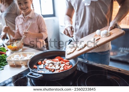 Cropped image of cute little girl and her beautiful parents cooking together in kitchen at home
