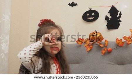a girl with a vampire make-up, boy in a zombie costume eating scary sweets, candy eyes spiders. trick or treat on Halloween. Funny kids in carnival costumes indoors. Cheerful children play with candy