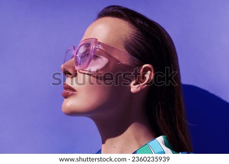 Profile portrait of a beautiful model in trendy square pink sunglasses with glossy make up posing against violet background.  Stylish glasses. Glance glamour picture. Summer Eye wear fashion 
