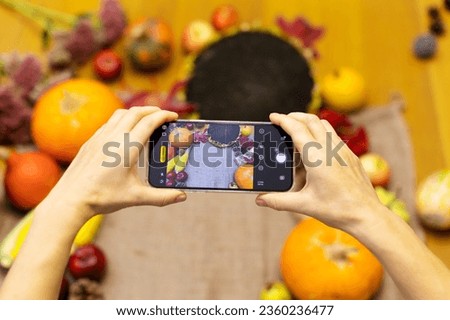 Women's hands hold the phone and take pictures of autumn offshoots on the table. Autumn composition, autumn background.Ofoshchi on the table, pumpkins, sunflowers, flowers, apples, hands.