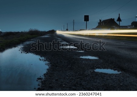 An evening scene featuring illuminated street and traffic signs surrounded by puddles of water