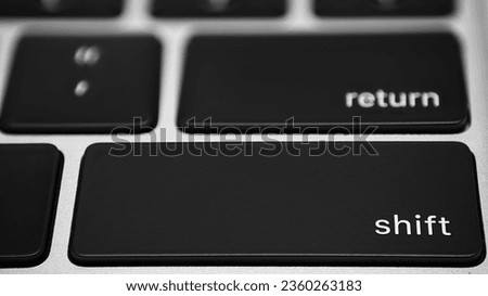 Macro close-up shot of a Shift button on a black keyboard on a silver metallic background.