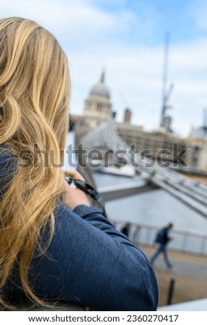 A blonde, female photographer capturing the iconic St Paul's Cathedral along the millennium Bridge, above the River Thames in London.