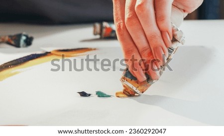 Drawing process. Artistic equipment. Unrecognizable woman painter hands squeezing paint out of tube creating picture in studio.