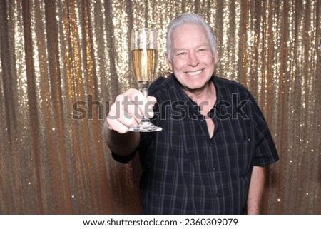 Photo Booth. Champagne. A man smiles and Toast to friends and family with a glass of Champagne while having his pictures taken in a Photo Booth. Champagne is Perfect for all Photo Booths. Cheers. 