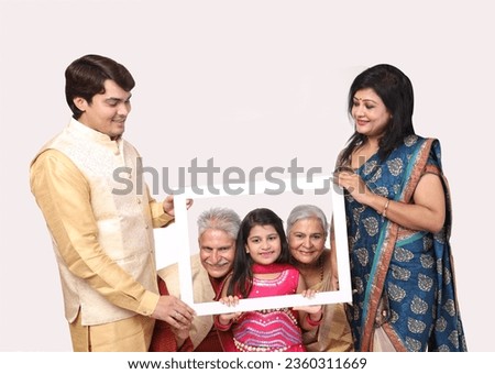 Indian happy family  holding photo frame shaped white carboard. grand parents with grand daughter showing face in photo frame isolated in white background. wearing traditional festive theme.
