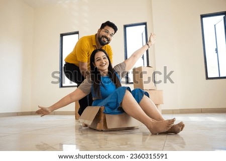 Happy young indian couple having fun in new home. Playing with boxes, Real estate, residential mortgage, moving into dream house concept. Royalty-Free Stock Photo #2360315591