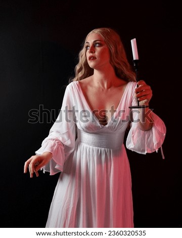 Close up portrait of scary blonde  vampire bride wearing elegant  white halloween fantasy gown. Isolated on dark  studio background with angsty gestural hands reaching out 