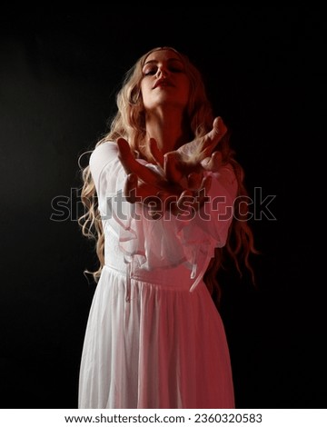 Close up portrait of scary blonde  vampire bride wearing elegant  white halloween fantasy gown. Isolated on dark  studio background with angsty gestural hands reaching out 