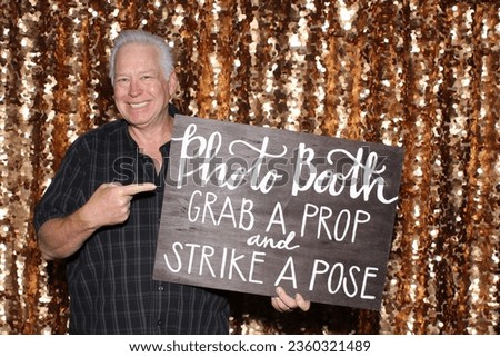 Photo Booth. Photo Booth Sign. A man smiles as he holds and points to a Sign that says to Grab a Prop and Strike a Pose while in the Photo Booth. Photo Booths are great fun for all Parties and events.