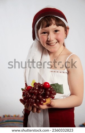 Portrait of Little girl in a stylized Tatar national costume with berries and a brush of grapes on a white background in the studio. Photo shoot of funny young teenager who is not professional model