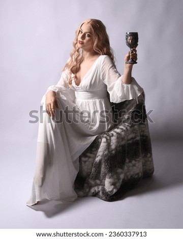 Full length portrait  of blonde woman  wearing  white historical bridal gown fantasy costume dress.  Seated pose with gestural hands reaching out, isolated on studio background.