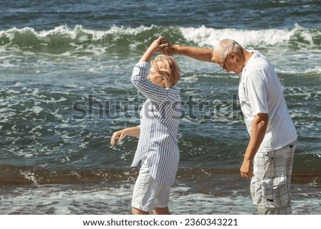 Happy elderly couple dancing on the seashore. In the background, the shore and sea waves.