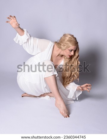 Full length portrait  of blonde woman  wearing  white historical bridal gown fantasy costume dress.  Sitting on floor posing with gestural hands reaching out, isolated on studio background.