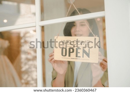 Woman hanging open sign on door, Store owner turning open sign broad through the door glass and ready to service.