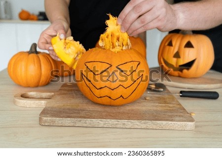 Man and woman gutting Halloween pumpkin. Couple of people hollowing Jack-o'-lantern, removing guts and seeds from a Halloween pumpkin by reaching inside through the cut-off top lid.