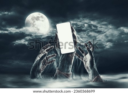 Zombie hands rising out of the ground, one is holding a smartphone with blank screen Royalty-Free Stock Photo #2360368699