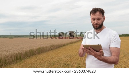 Agriculture. An agronomist stands with a tablet in a wheat field, a combine works in the background. A combine harvester harvests wheat in a farmer's field.