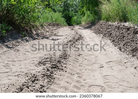 Sand road in the forest. Tire pattern of quad bike on driveway. Track imprint of quadricycle on nature land. Sand texture off road. Path in forest close up. Sand mounds and green forest in sunny day. Royalty-Free Stock Photo #2360378067