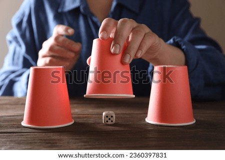 Woman playing thimblerig game with red cups at wooden table, closeup Royalty-Free Stock Photo #2360397831