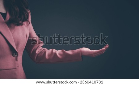 Beautiful asian woman in pink suit hand showing empty copy space for product, text or message on over isolated black background. Concept of advertising, product, sale promotion, presentation. 