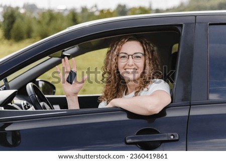young beautiful smiling woman in car looking straight to camera, holding car alarm keychain in hand, attractive caucasian woman in white t-shirt
