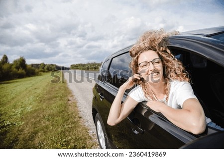 young beautiful smiling woman sitting in car in passenger seat while traveling, hair fluttering in wind, attractive caucasian woman in white t-shirt