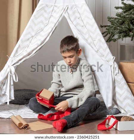 Family Christmas. Children open Christmas presents. A teenage boy opens a gift and smiles while sitting on the floor of a house decorated for New Year and Christmas