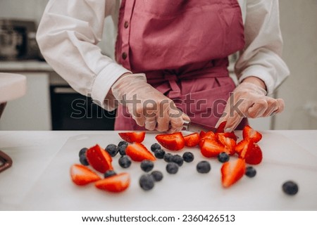 Woman confectioner in an apron decorating a cherry cake with cherries, a Homemade birthday cake. Summer fruit cake, vegan dessert, Selective focus. High quality photo