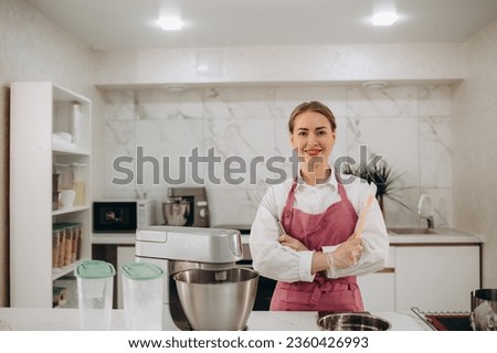 Pastry chef confectioner young caucasian woman with kitchen spatula whisk and cake on kitchen table. Cakes cupcakes and sweet dessert.  Royalty-Free Stock Photo #2360426993