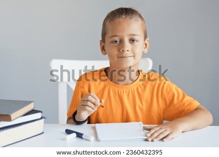 Portrait of male little pupil writing at desk in classroom at the elementary school. Student boy study doing homework and preparing fot test at home. Education knowledge concept.