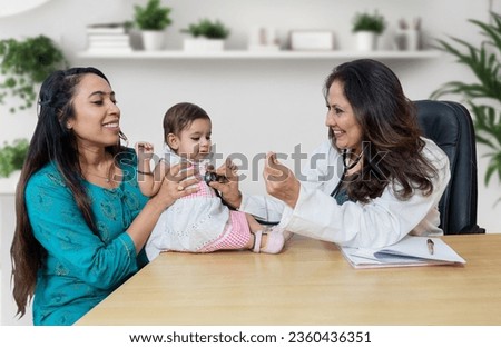 Young indian mother with her cute little baby visiting general pediatrician in modern clinic for routine check-up, Healthcare and medical concept. Royalty-Free Stock Photo #2360436351