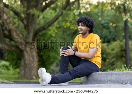 A young Indian man does sports in the park, takes a morning walk. Got a leg injury, is holding his knee, is in pain. Royalty-Free Stock Photo #2360444295