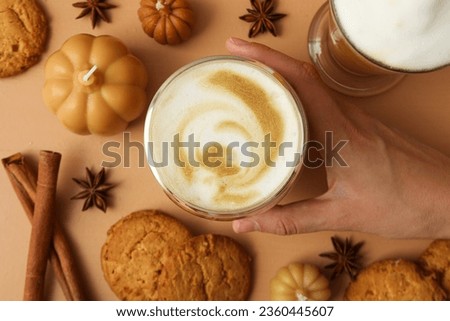 Pumpkin coffee, female hand, spices, cookies and candles on beige background, top view